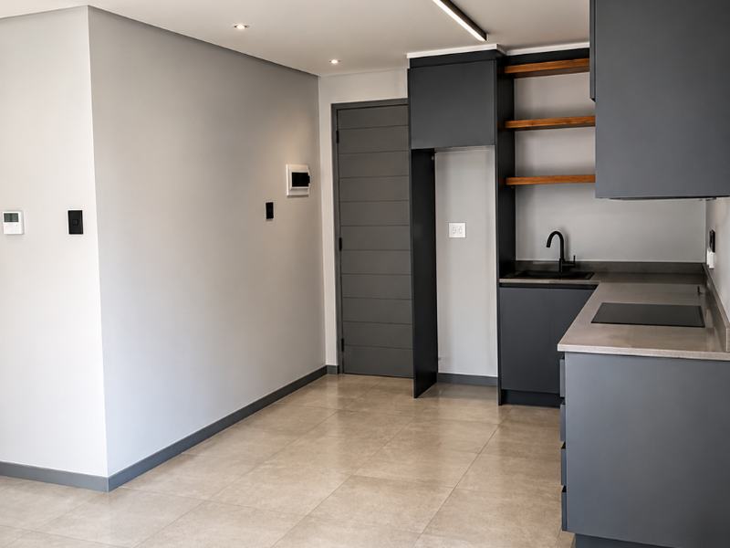 Modern kitchen featuring dark grey cabinetry, stone countertops, open shelving, and integrated hob, set against a neutral interior with tiled flooring.