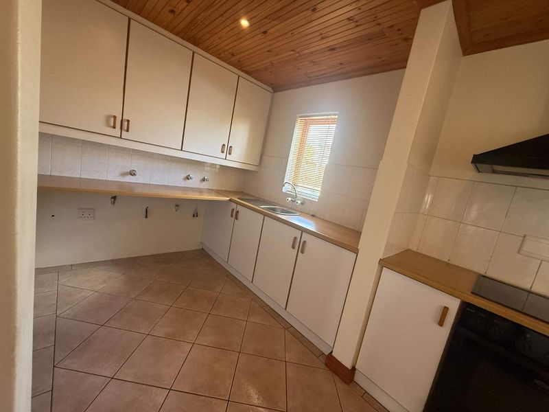 A functional kitchen featuring built-in cabinetry, laminate countertops, a stainless steel sink, and a timber ceiling, offering a practical layout for renovation.