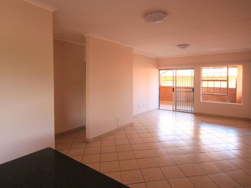 An empty, open-plan living area featuring neutral tiled flooring, flush mount lighting, and a sliding glass door leading to an outdoor balcony.