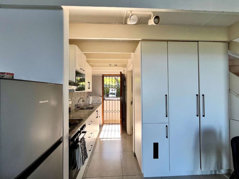 A functional galley-style kitchen featuring built-in cabinetry, stone countertops, and integrated appliances, leading directly to an exterior entrance with a security gate.