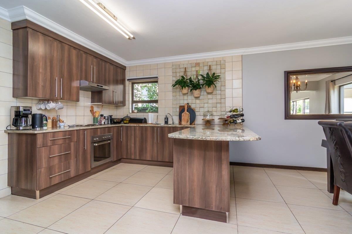 A functional kitchen featuring wood-finish cabinetry, granite countertops, a built-in oven, extractor fan, and tiled flooring with a breakfast bar peninsula.
