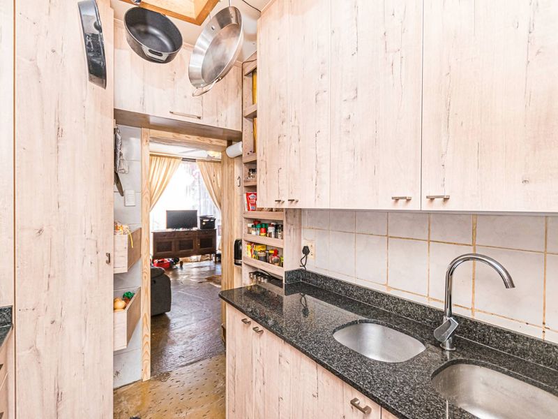 Compact kitchen featuring light wood-look cabinetry, granite countertops, and a double stainless steel sink with a tiled backsplash.