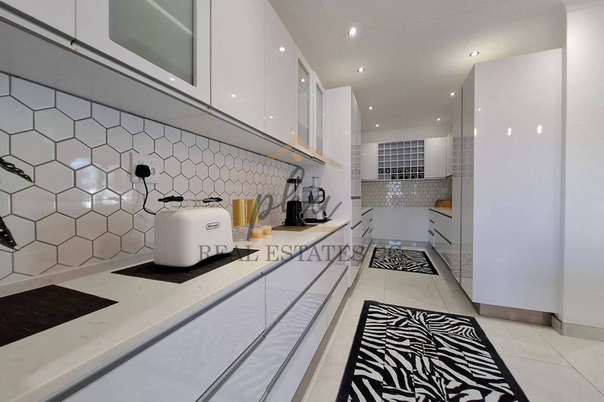 Modern galley-style kitchen featuring high-gloss white cabinetry, stone countertops, and a stylish hexagonal tile backsplash with integrated recessed lighting.