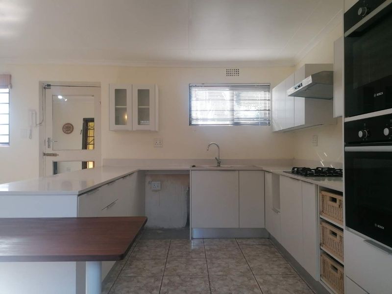 A functional kitchen featuring white cabinetry, stone countertops, built-in oven, gas hob, and tiled flooring, with an open space for an under-counter appliance.