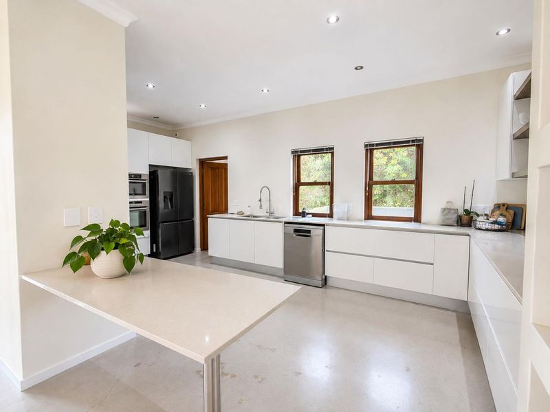 Modern kitchen featuring sleek handleless white cabinetry, quartz countertops, polished concrete floors, and high-end built-in appliances with ample natural light.