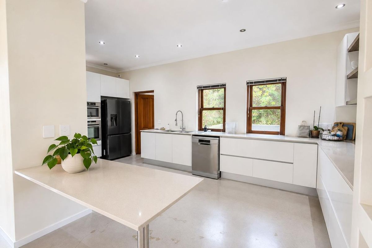 Modern kitchen featuring sleek handleless white cabinetry, quartz countertops, polished concrete floors, and high-end built-in appliances with ample natural light.