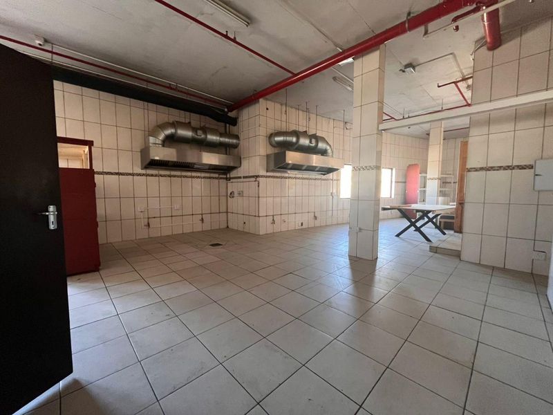 Spacious industrial kitchen area featuring tiled surfaces, stainless steel extractor hoods, and exposed fire suppression infrastructure, suitable for commercial food preparation.