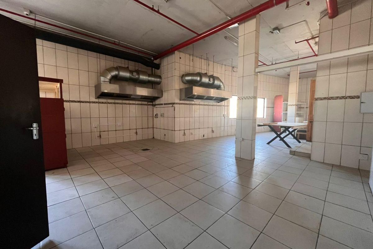 Spacious industrial kitchen area featuring tiled surfaces, stainless steel extractor hoods, and exposed fire suppression infrastructure, suitable for commercial food preparation.