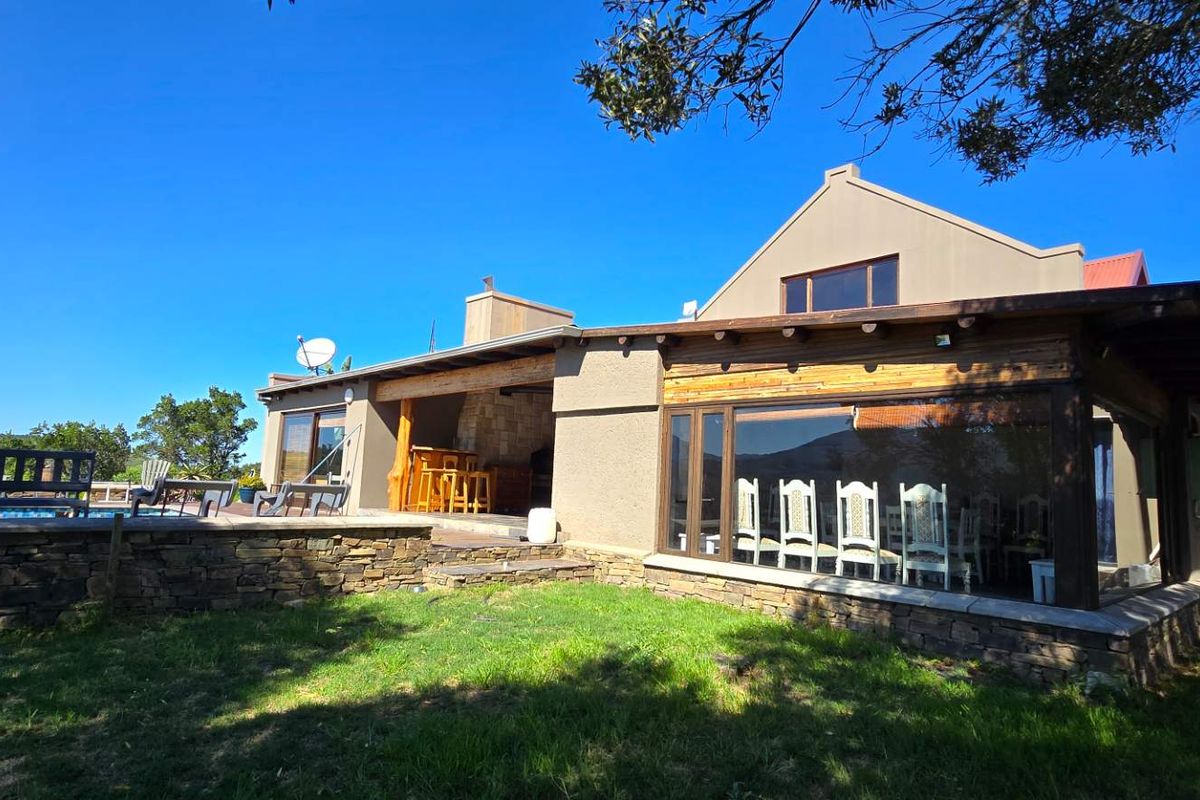 Rear view of the farm property featuring a covered patio area, stone retaining walls, and large glass windows overlooking the garden.