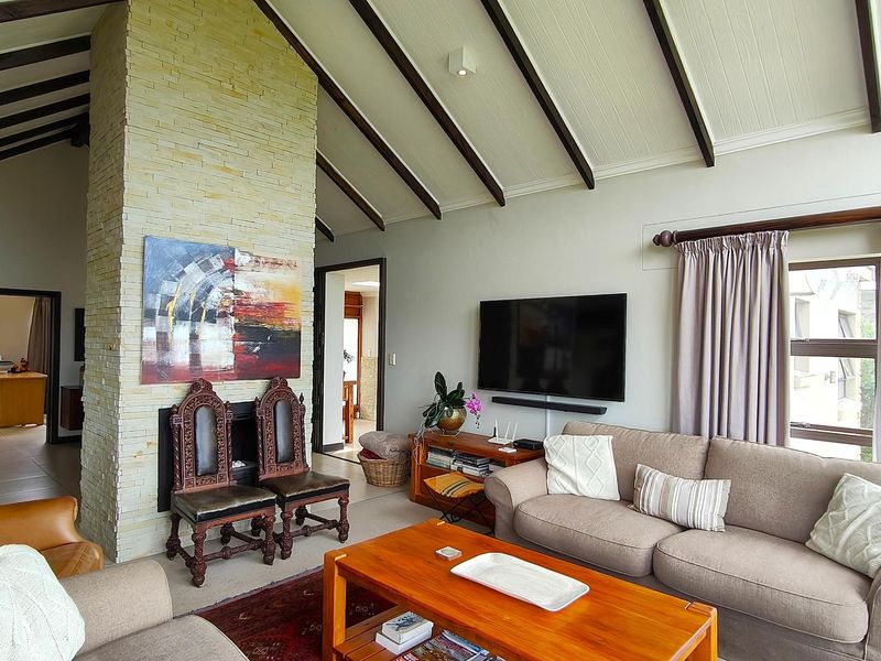 Spacious living room featuring a vaulted ceiling with exposed timber beams and a prominent stone-clad fireplace, creating a warm and inviting atmosphere.