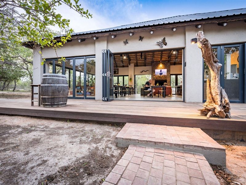 Spacious timber deck patio featuring bi-fold doors leading into an open-plan living area with a brick fireplace and exposed beam ceiling.
