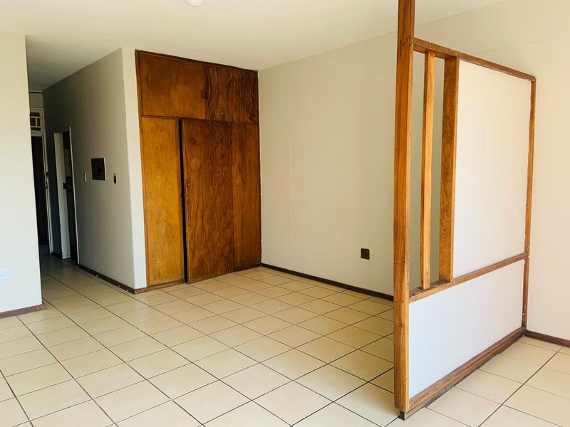 An empty living area featuring ceramic floor tiles, a built-in wooden storage unit, and a decorative wooden room divider.