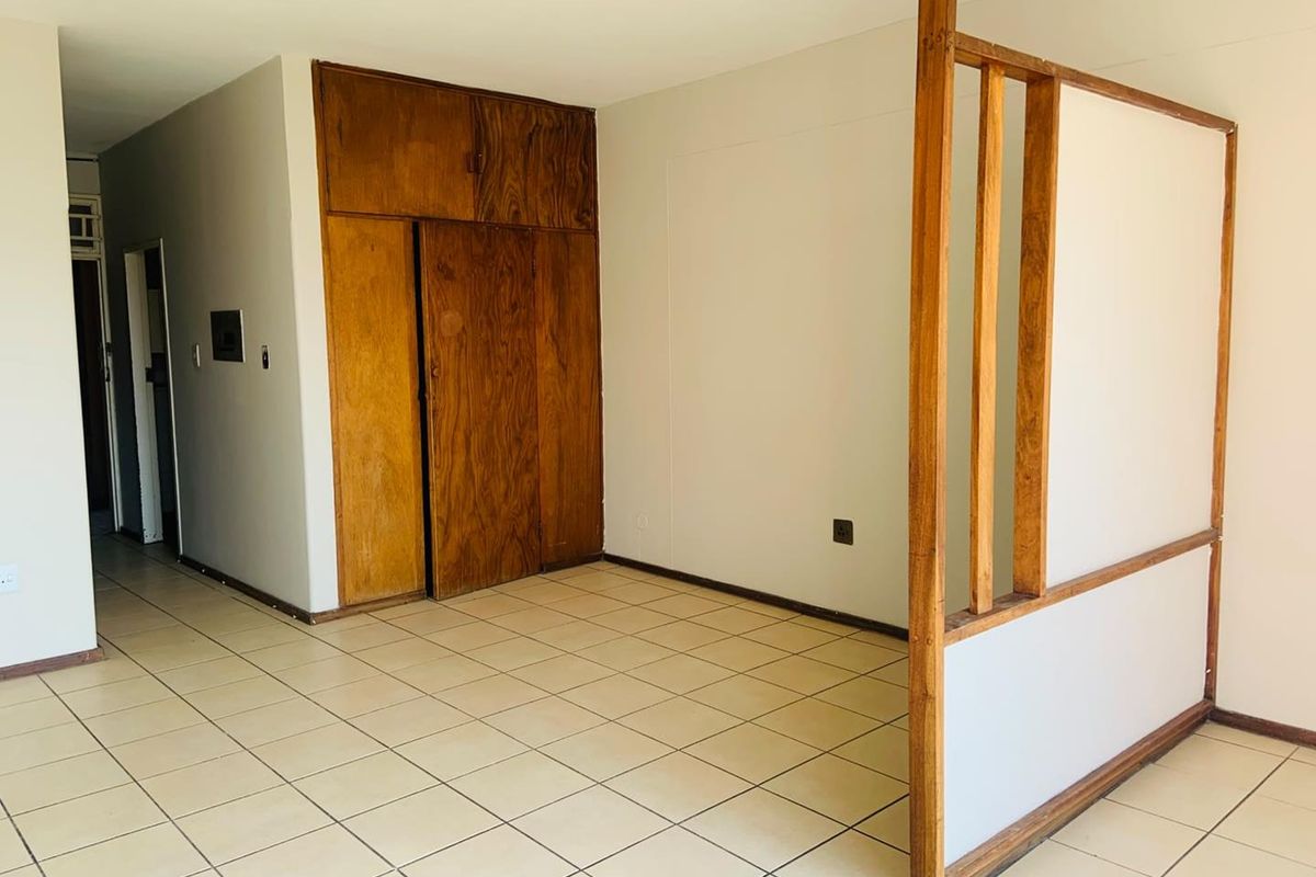 An empty living area featuring ceramic floor tiles, a built-in wooden storage unit, and a decorative wooden room divider.