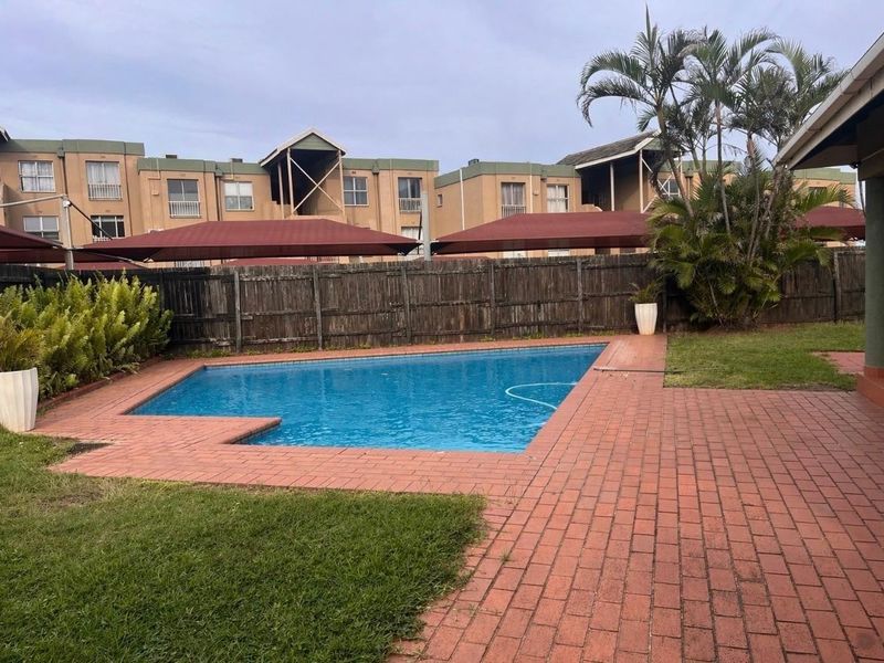 Outdoor pool area featuring a swimming pool, brick paved surround, and timber boundary fencing within a residential apartment complex.