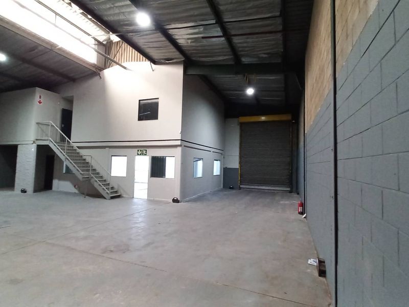 Spacious industrial warehouse featuring a high-clearance ceiling, roller shutter door, mezzanine level with office space, and concrete flooring.