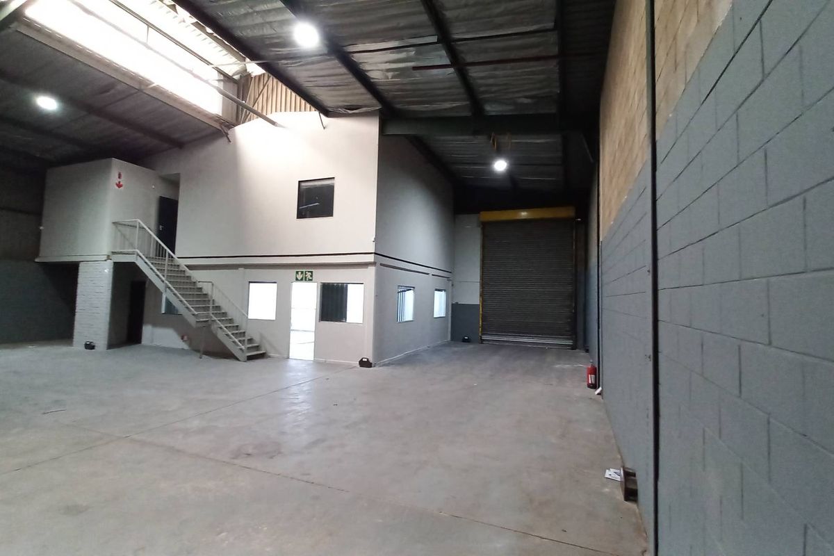 Spacious industrial warehouse featuring a high-clearance ceiling, roller shutter door, mezzanine level with office space, and concrete flooring.