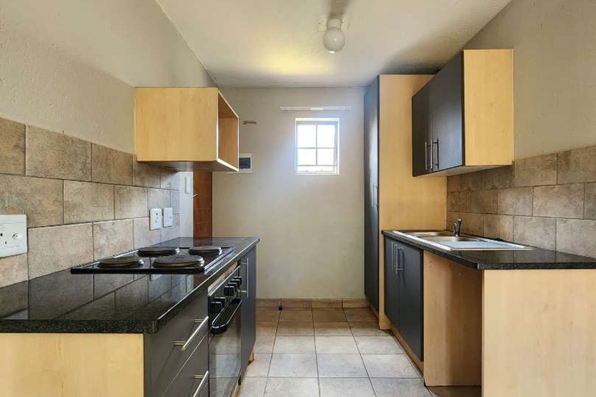 A functional galley-style kitchen featuring built-in cabinetry, granite countertops, an integrated electric hob and oven, and tiled flooring throughout.