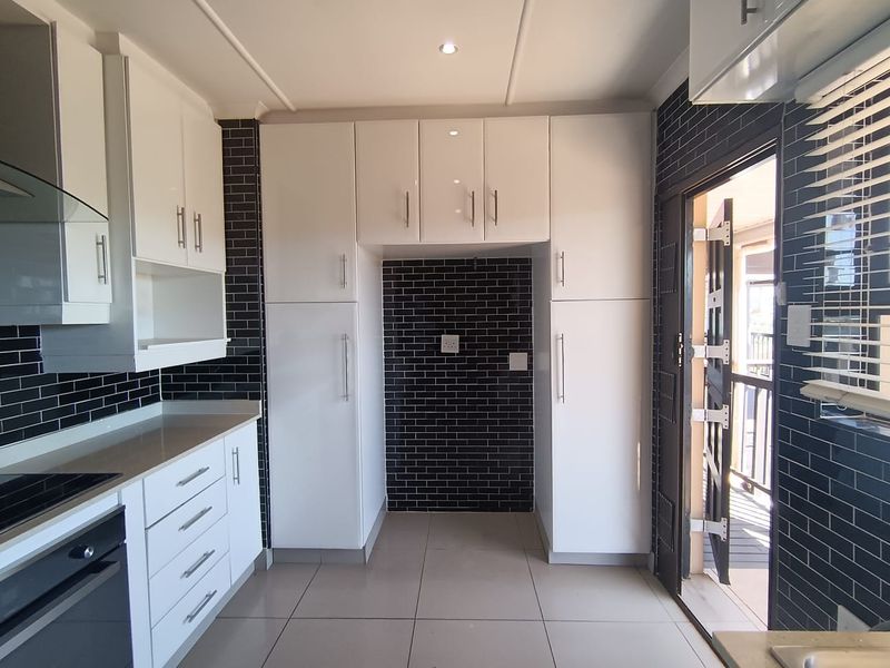 Modern kitchen featuring white cabinetry, dark subway tile backsplash, ceramic floor tiles, and built-in appliances, with direct access to an outdoor area.