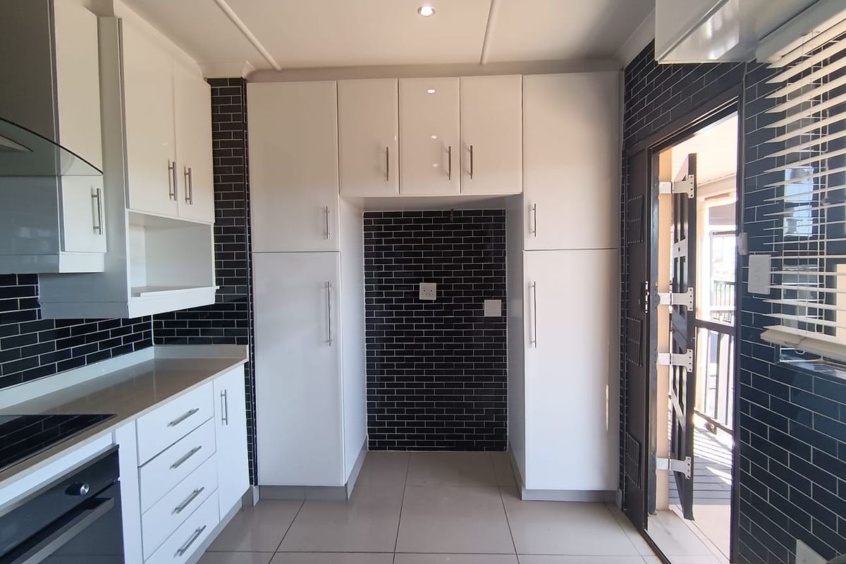 Modern kitchen featuring white cabinetry, dark subway tile backsplash, ceramic floor tiles, and built-in appliances, with direct access to an outdoor area.