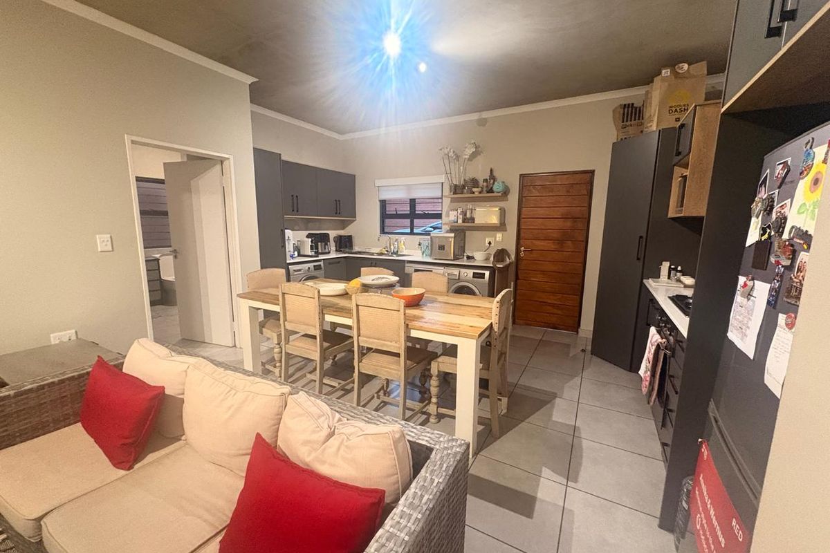 Open-plan kitchen and dining area featuring modern dark cabinetry, tiled floors, and direct access to adjacent rooms.