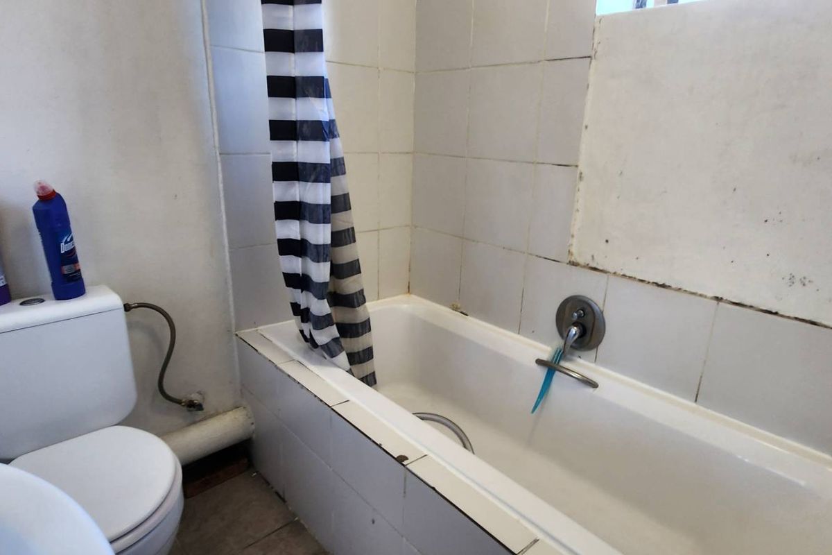 A dated bathroom featuring a standard bathtub with shower mixer and a close-coupled toilet, requiring cosmetic updates and tile repairs.