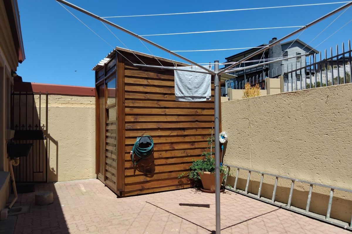 A rear courtyard area featuring a timber storage shed, paved flooring, and a rotary clothesline against a rendered boundary wall.