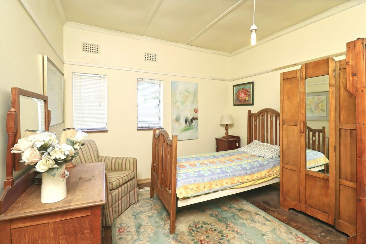 A bedroom featuring timber flooring, high ceilings with picture rails, and dual windows providing natural light.