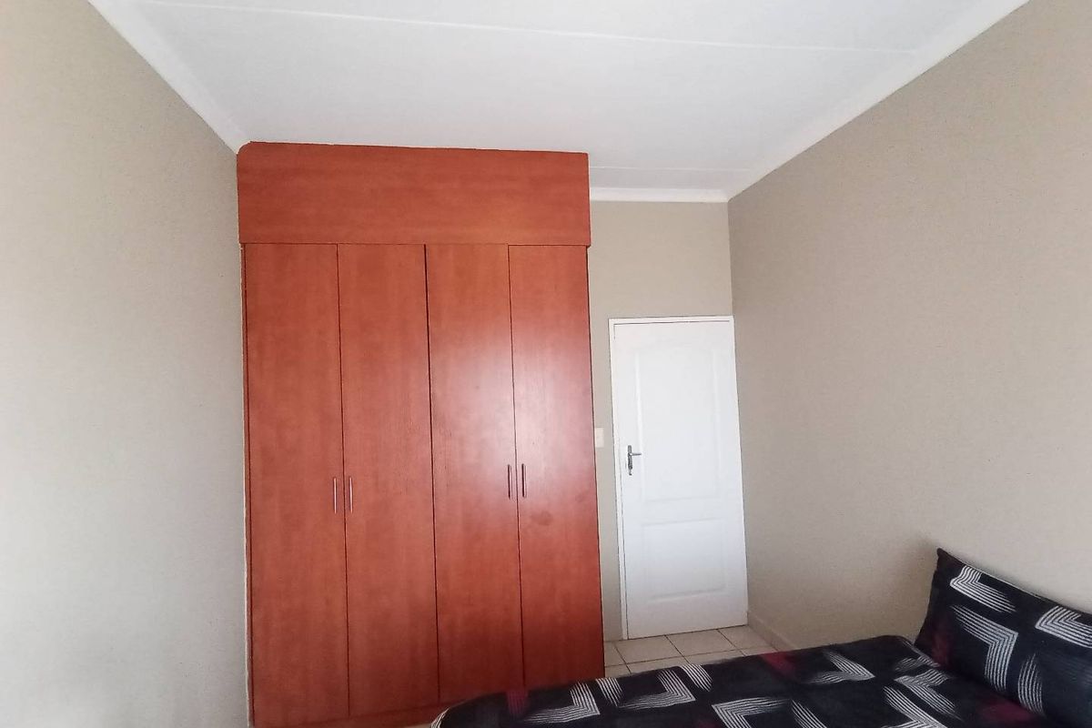 A bedroom featuring built-in wooden cupboards and tiled flooring, providing functional storage space within the room.