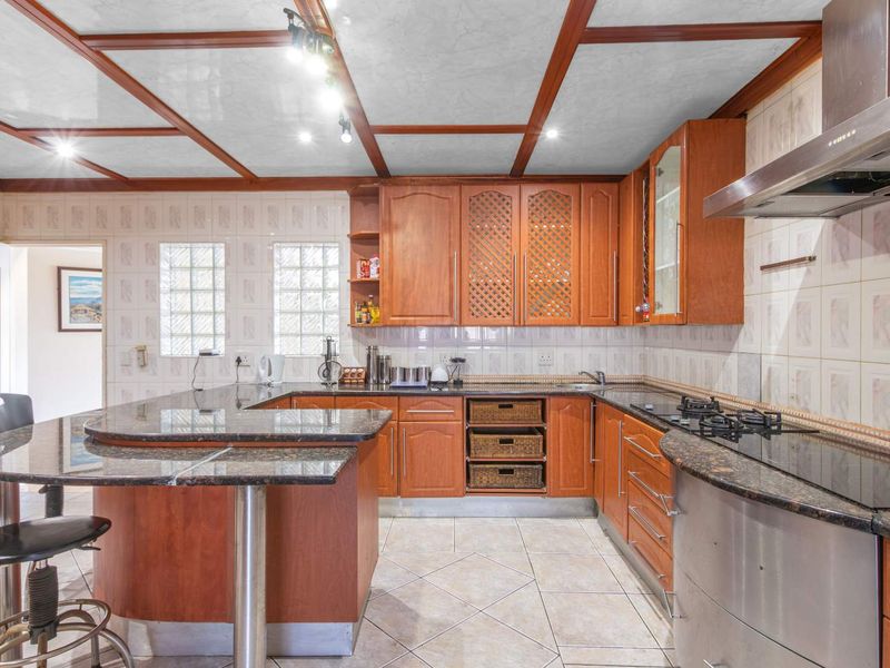 A functional kitchen featuring wooden cabinetry, granite countertops, a gas hob with extractor fan, and a breakfast bar, complemented by a coffered ceiling.