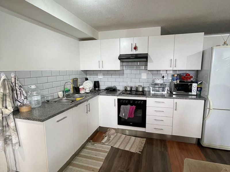 A functional kitchen featuring white cabinetry, grey subway tile backsplash, granite-look countertops, and integrated appliances, complemented by durable laminate wood flooring.