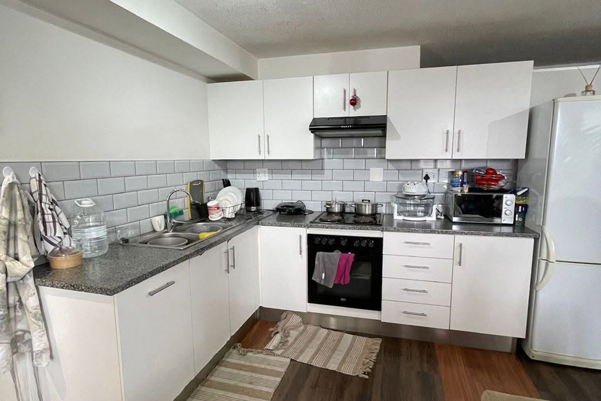 A functional kitchen featuring white cabinetry, grey subway tile backsplash, granite-look countertops, and integrated appliances, complemented by durable laminate wood flooring.