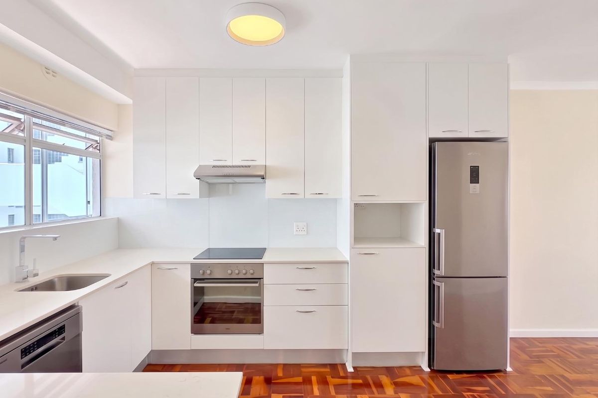 Modern kitchen featuring white cabinetry, stone countertops, stainless steel appliances, and classic parquet flooring, offering a clean and functional cooking space.