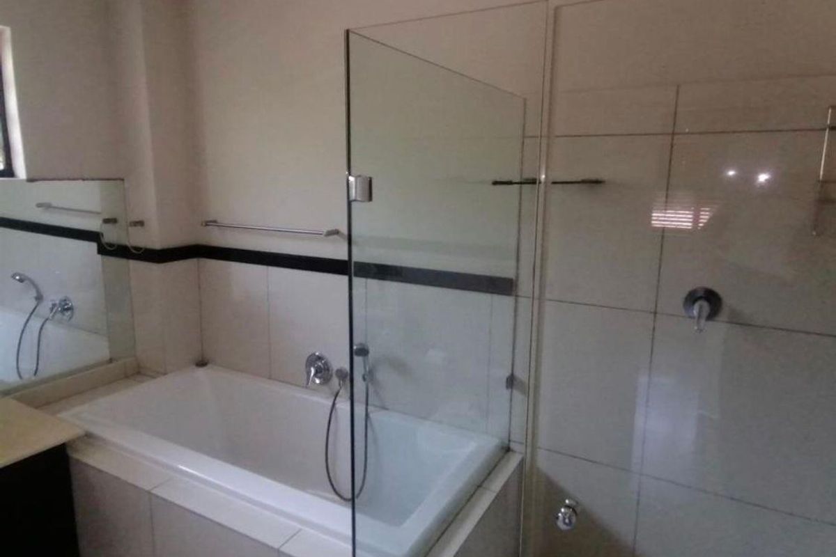 A clean, modern bathroom featuring a built-in bathtub, a glass shower screen, and neutral wall tiling with a decorative black accent border.