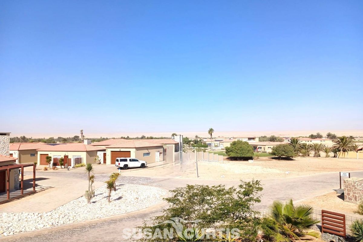 An elevated view of a residential estate featuring paved roads, landscaped garden areas, and surrounding desert landscape.