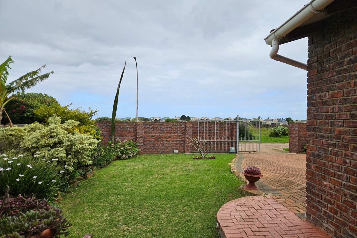 A well-maintained rear garden featuring a brick boundary wall, metal gate, and paved driveway area adjacent to the main house structure.