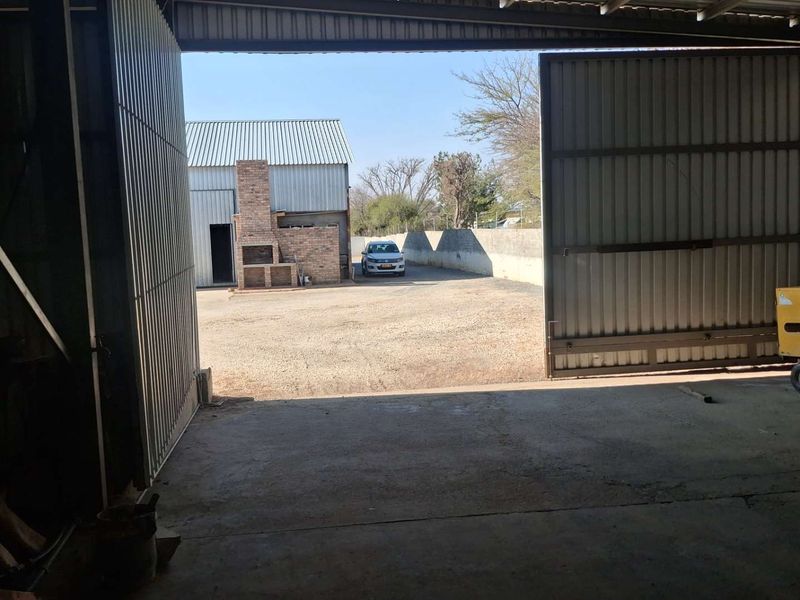 Spacious industrial garage with large sliding doors opening onto a paved yard featuring a brick braai area.