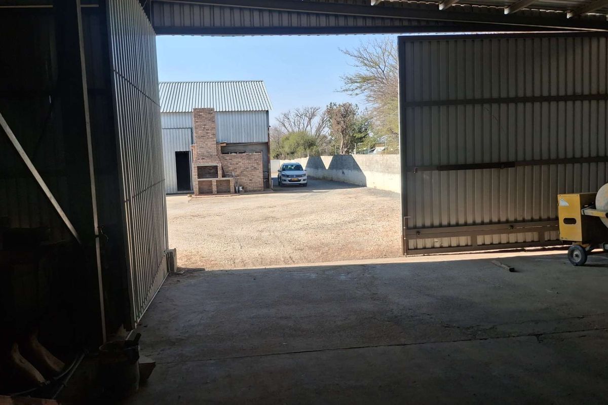 Spacious industrial garage with large sliding doors opening onto a paved yard featuring a brick braai area.