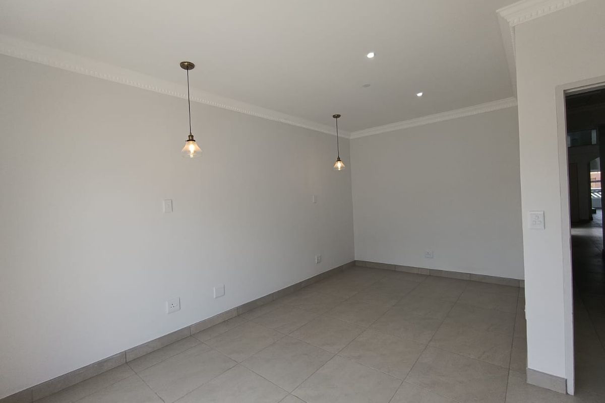 A bright, empty living area featuring neutral tiled flooring, decorative crown molding, and modern pendant lighting.