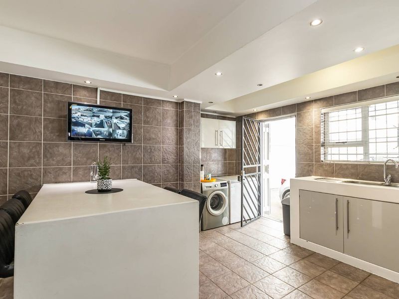 A functional scullery area featuring tiled walls and flooring, built-in cabinetry with a sink, and direct access to the exterior via a security gate.