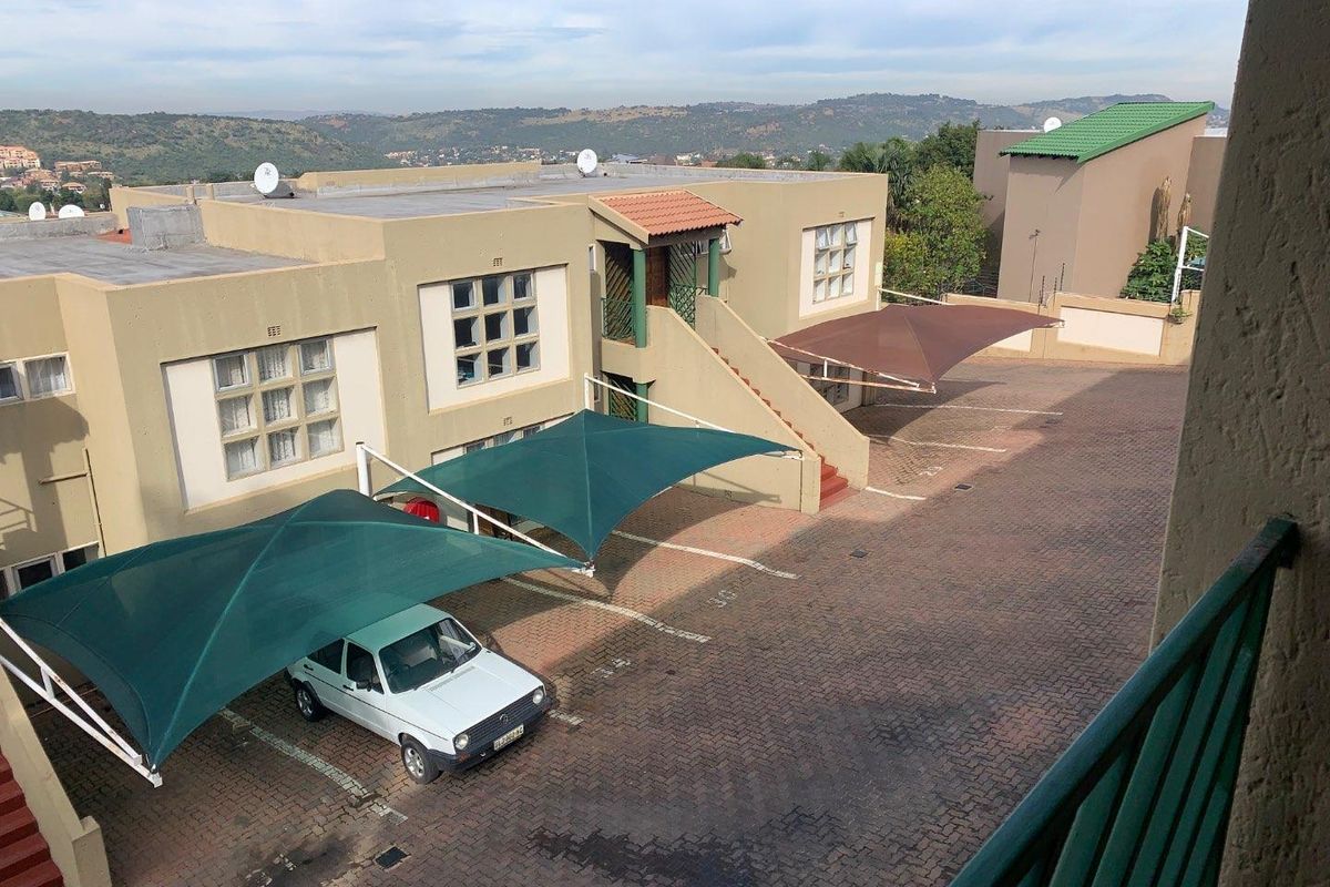 Elevated view of the apartment complex exterior, featuring paved parking areas with shade cloth carports and surrounding residential landscape.