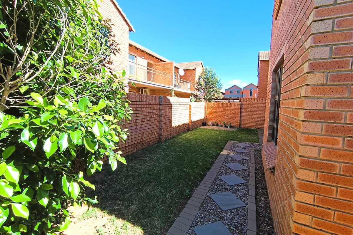 A private rear garden area featuring a well-maintained lawn, a stone paver pathway, and face brick boundary walls.