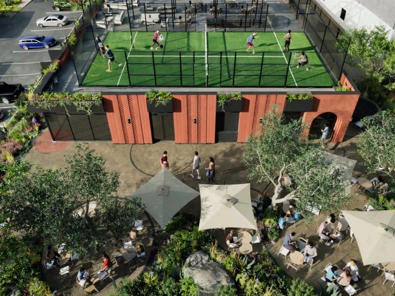 Aerial view of a modern industrial complex featuring a rooftop padel court, landscaped courtyard with outdoor seating, and adjacent parking facilities.