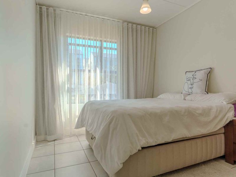 A bright bedroom featuring neutral tiled flooring and floor-to-ceiling curtains providing access to an outdoor area.