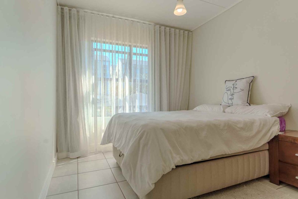 A bright bedroom featuring neutral tiled flooring and floor-to-ceiling curtains providing access to an outdoor area.