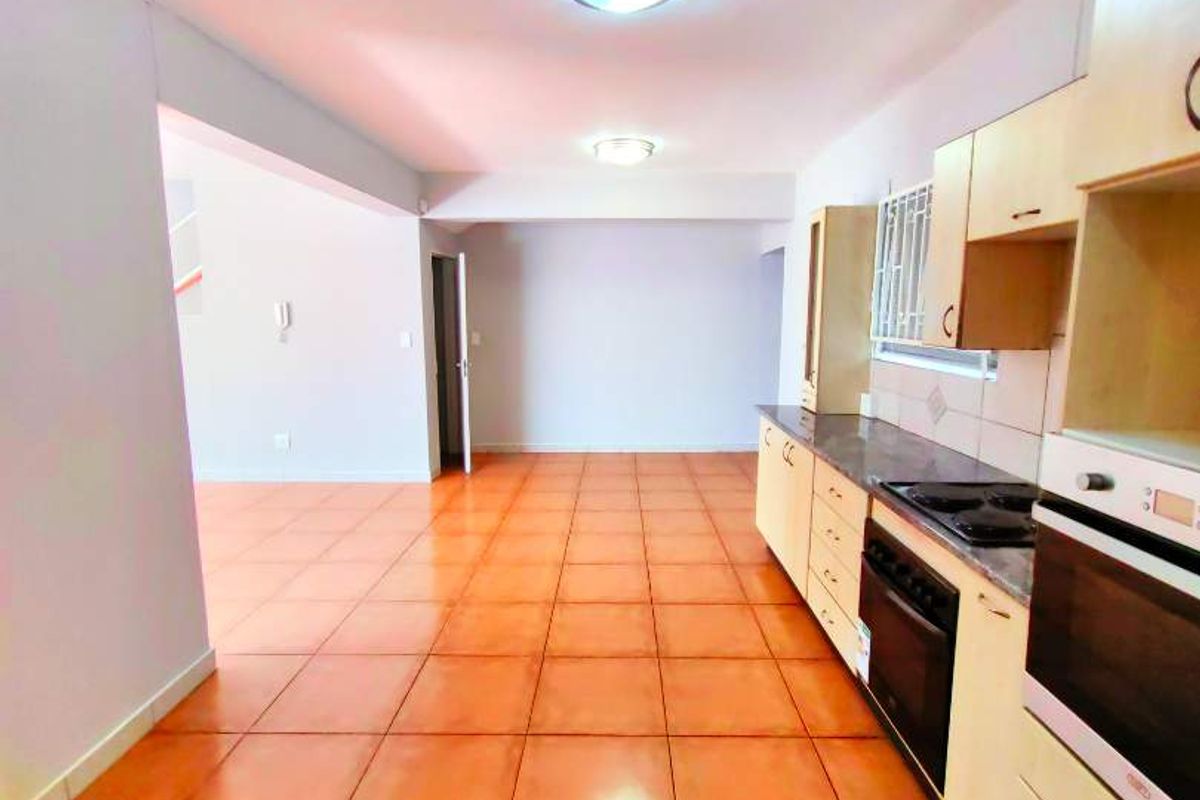 An open-plan kitchen featuring built-in cabinetry, an integrated oven and hob, and ceramic floor tiles, leading into an adjacent living area.