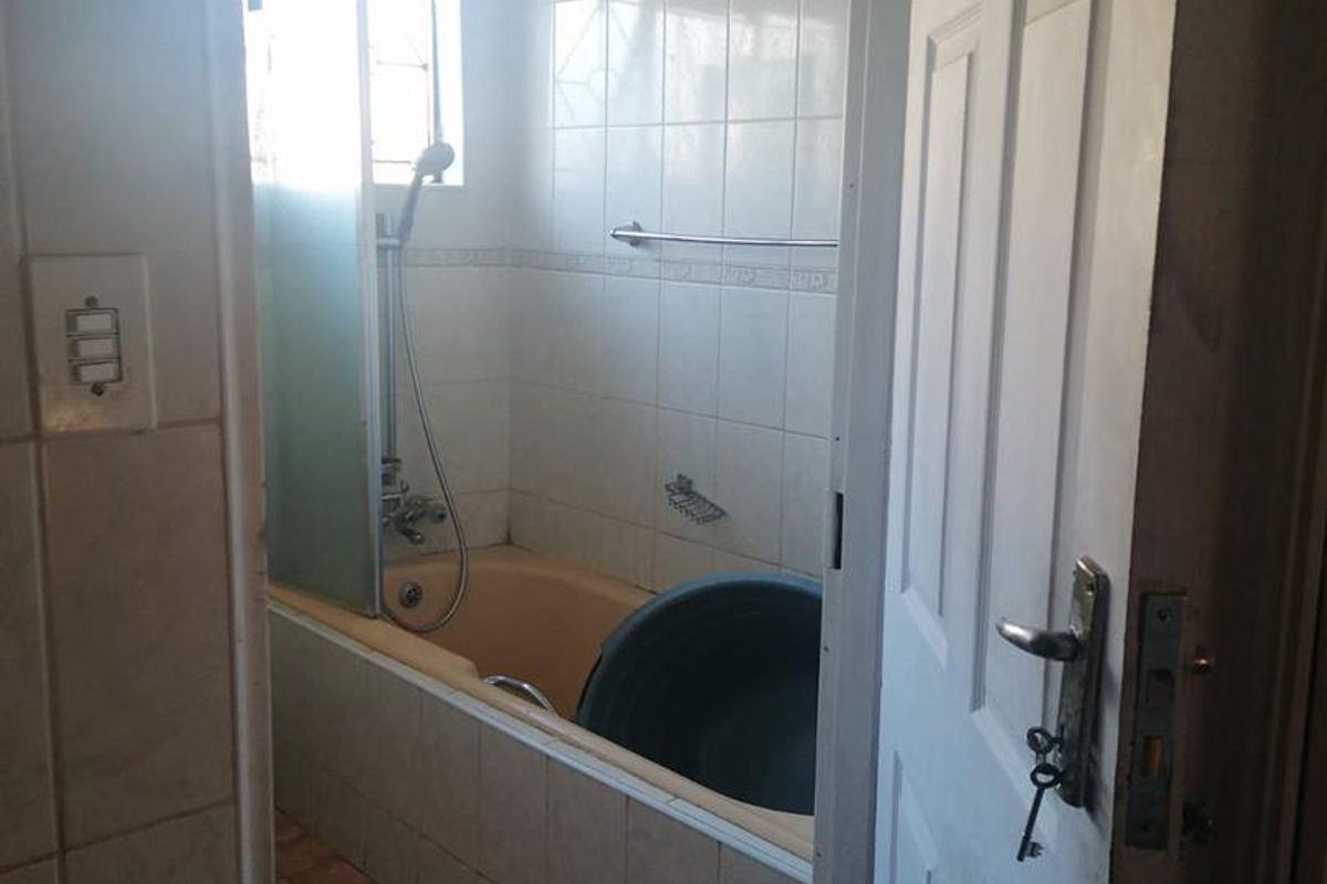 A dated bathroom featuring a built-in bathtub with shower attachment, tiled walls, and ceramic floor tiles.