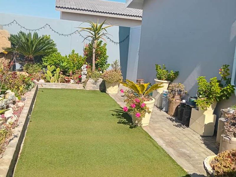 A well-maintained rear garden area featuring an artificial lawn, paved walkway, and perimeter boundary walls.