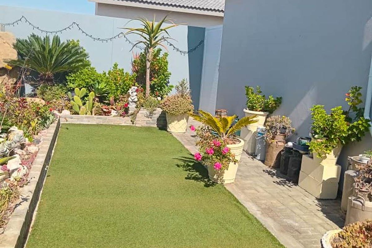 A well-maintained rear garden area featuring an artificial lawn, paved walkway, and perimeter boundary walls.
