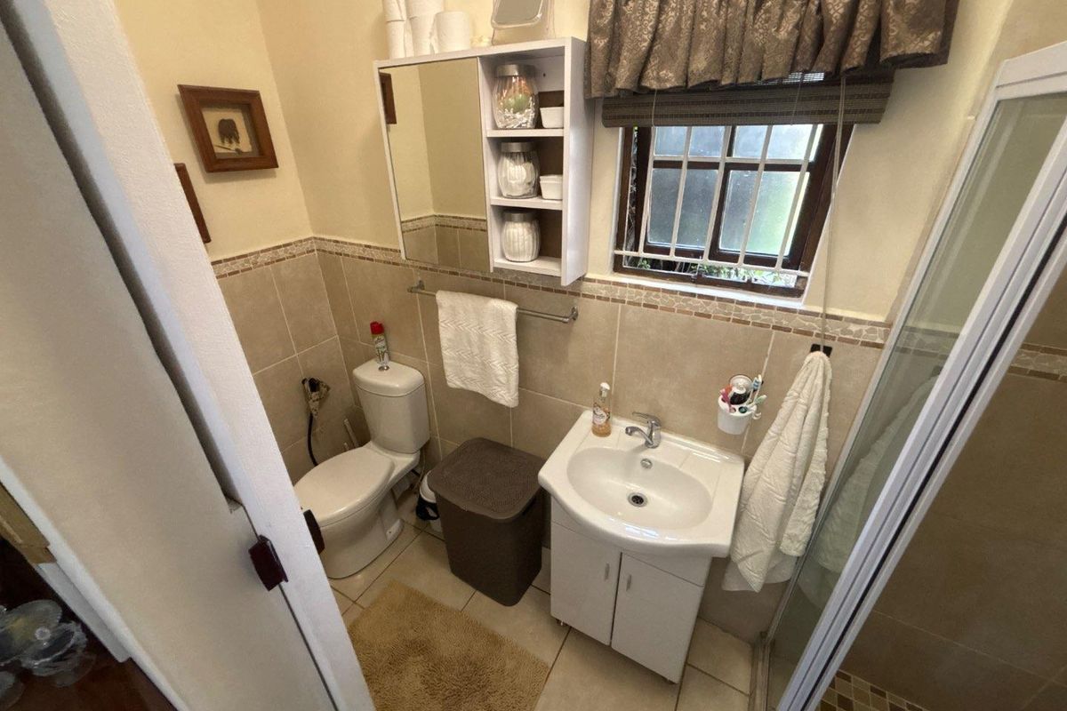 A compact bathroom featuring a vanity basin, toilet, and shower enclosure with neutral wall and floor tiling.