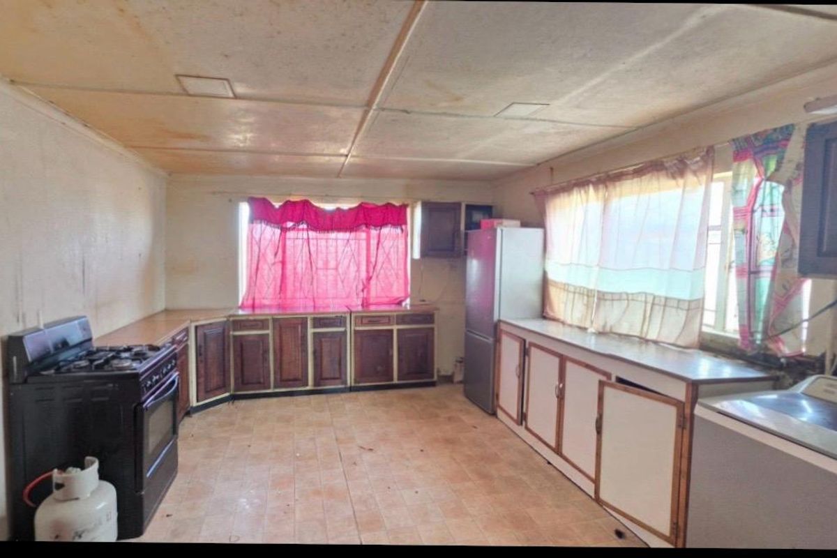 A dated kitchen featuring original cabinetry, tiled flooring, and a drop ceiling, offering significant potential for a modern renovation.